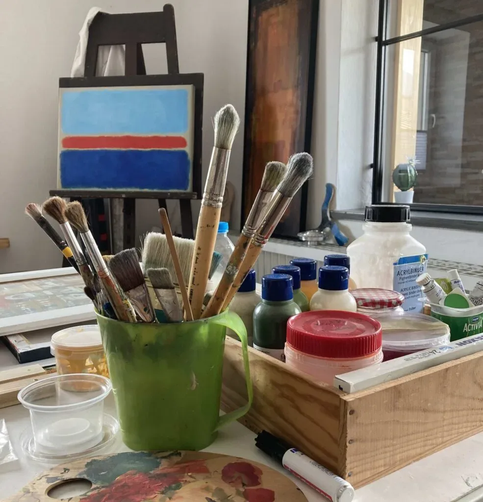 Malutensilien und Leinwand in einem Atelier, Pinsel und Farben im Vordergrund.